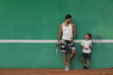 Father with his son near green wall on tennis court. Space for text