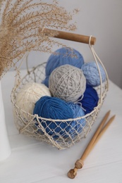 Woolen yarns in basket and knitting needles on white wooden table