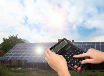 Woman using calculator against house with installed solar panels. Renewable energy and money saving
