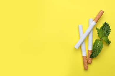 Menthol cigarettes and mint on yellow background, flat lay. Space for text