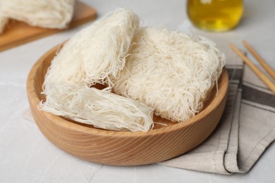 Photo of Wooden bowl with uncooked rice noodles on light table, closeup