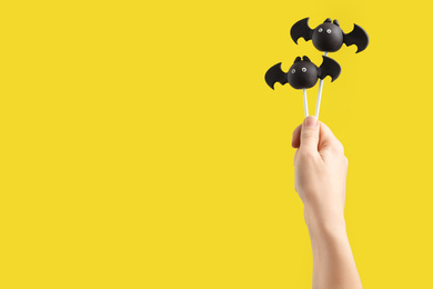 Woman with delicious bat shaped cake pops and space for text on yellow background, closeup. Halloween celebration