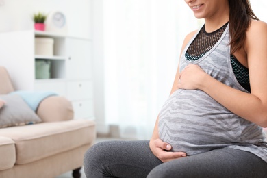 Young pregnant woman in fitness clothes at home, closeup. Space for text