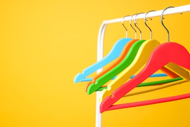 Bright clothes hangers on metal rack against yellow background, closeup. Space for text