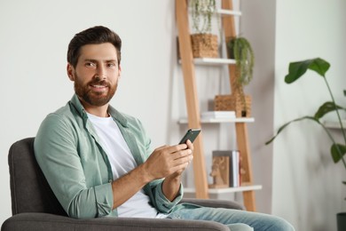 Photo of Handsome man with smartphone at home, space for text