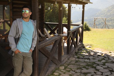 Handsome man enjoying beautiful nature near house with wooden terrace