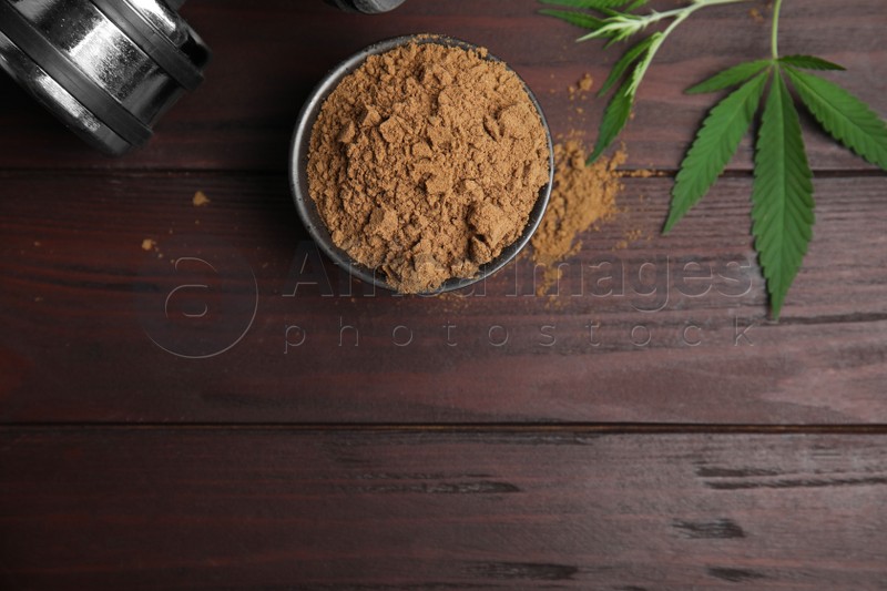 Hemp protein powder, fresh leaves and dumbbell on wooden table, flat lay. Space for text