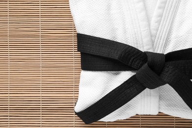 Martial arts uniform with black belt on bamboo mat, top view. Space for text
