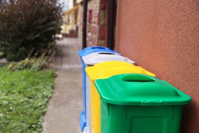 Photo of Many colorful recycling bins near brown wall outdoors