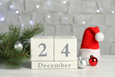 December 24 - Christmas Eve. Wooden block calendar and decor on white table against blurred festive lights