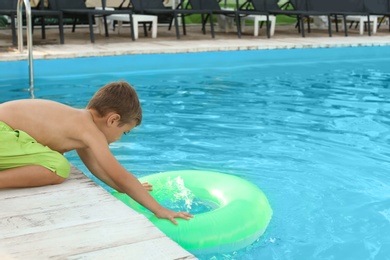 Little child reaching for inflatable ring in outdoor swimming pool. Dangerous situation