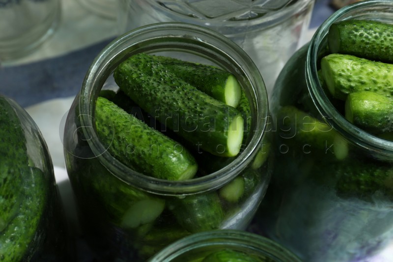 Photo of Glass jars with fresh ripe cucumbers on table, closeup. Pickling vegetables