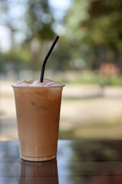 Photo of Plastic takeaway cup of delicious iced coffee on table in outdoor cafe