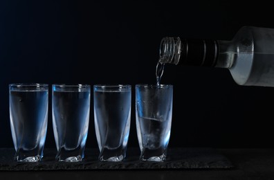 Pouring vodka from bottle in glass on black table