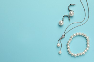 Photo of Elegant necklace, bracelet and earrings with pearls on light blue background, flat lay. Space for text