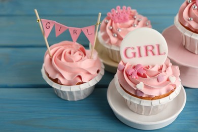 Delicious cupcakes with pink cream and toppers for baby shower on light blue wooden table