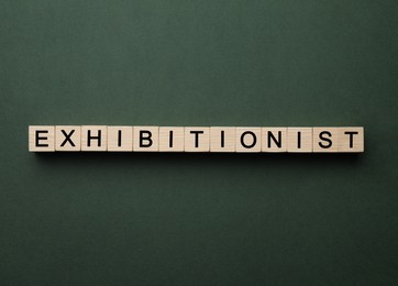 Photo of Word EXHIBITIONIST made with wooden cubes on dark green background, flat lay
