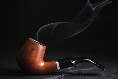 Stylish tobacco pipe with smoke on black table