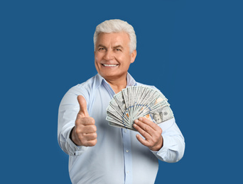 Happy senior man with cash money on blue background. Space for text