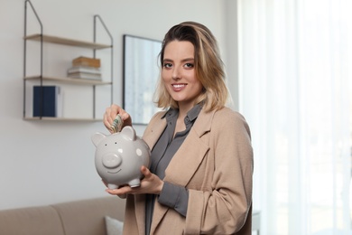 Businesswoman putting money into piggy bank indoors