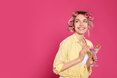 Young housewife with glass of martini on pink background. Space for text