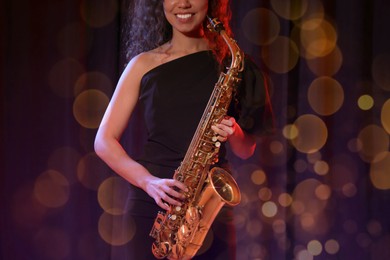 African American woman with saxophone on dark background. Bokeh effect