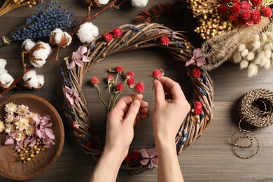 Florist making wreath with dried flowers at wooden table, top view
