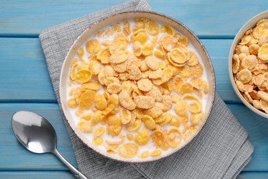 Photo of Bowl of tasty corn flakes served for breakfast on light blue wooden table, flat lay