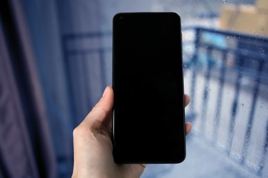 Photo of Woman holding smartphone with blank screen near window, closeup