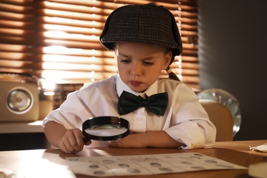 Cute little detective exploring fingerprints with magnifying glass at table in office