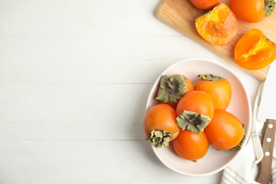 Delicious fresh persimmons on white wooden table, flat lay. Space for text