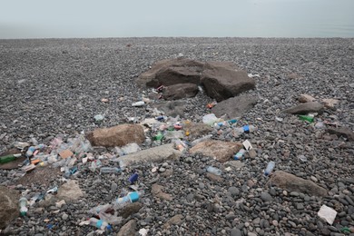 Photo of Garbage scattered on pebbles near sea. Recycling problem