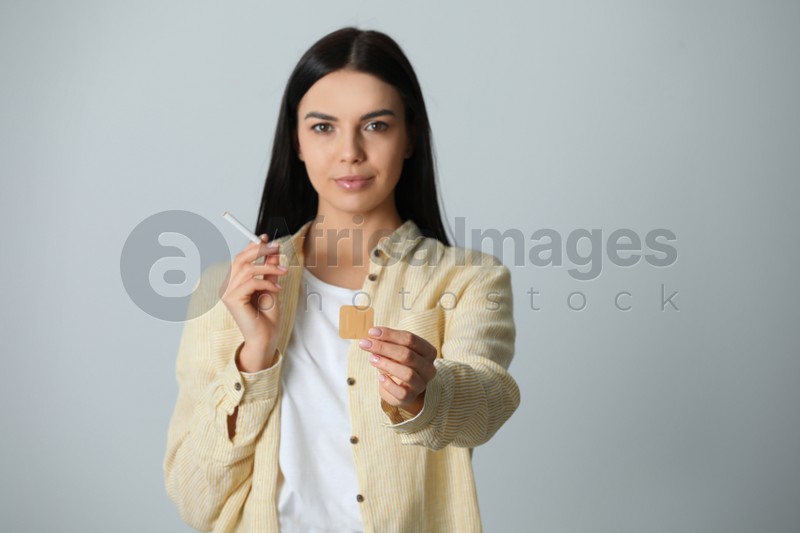Photo of Happy young woman with nicotine patch and cigarette on light grey background