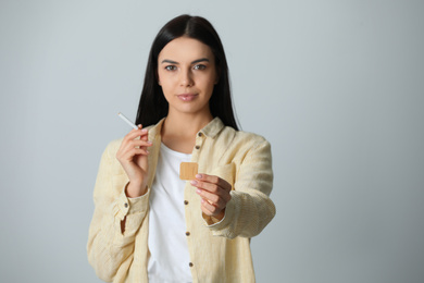 Happy young woman with nicotine patch and cigarette on light grey background