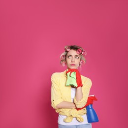 Young housewife with detergent and rag on pink background