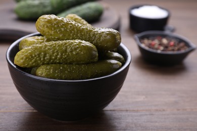 Bowl of pickled cucumbers and ingredients on wooden table, closeup