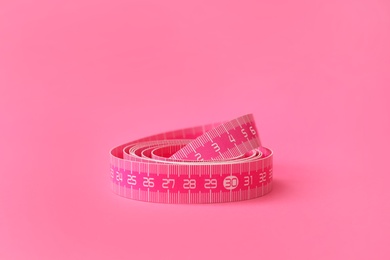 New measuring tape on pink background, closeup