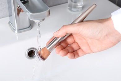 Woman washing makeup brush under stream of water in sink, closeup