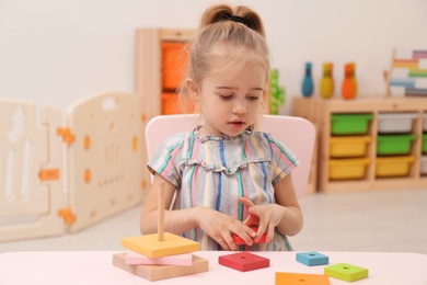 Cute child playing with colorful wooden stacker at table in room