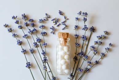 Bottle of homeopathic remedy and lavender on white background, flat lay