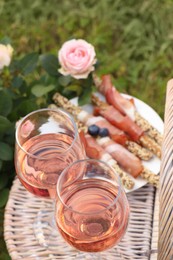 Flowers near glasses of delicious rose wine and food on picnic basket outdoors, closeup