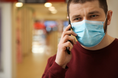 Photo of Man with disposable mask talking on phone indoors. Dangerous virus