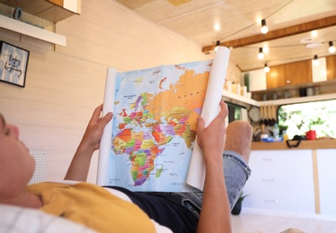 Young traveler with world map planning trip on bed in motorhome, closeup