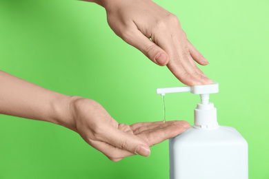 Photo of Woman applying antiseptic gel on hand against green background, closeup