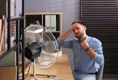 Man suffering from heat in front of fan at workplace