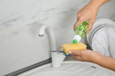 Woman pouring cleaning product for dish washing onto sponge near kitchen sink. Space for text