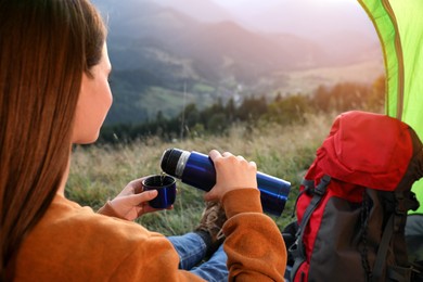 Young woman with thermos inside of camping tent in mountains