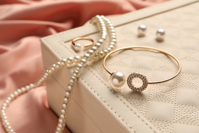 Photo of Box with luxurious pearl jewelry on pink fabric, closeup