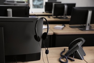 Stationary phone near modern computer with headset on wooden desk indoors. Hotline service