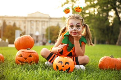 Cute little girl with pumpkin candy bucket wearing Halloween costume in park
